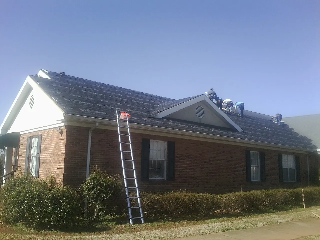 Crew tearing shingles off a brick ranch roof with a ladder set — Metal Roof Repair work by our crew in North Plains