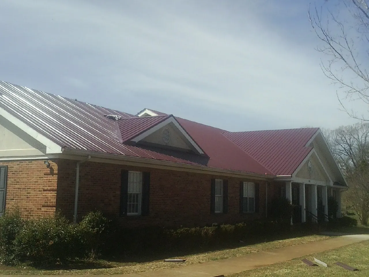 Red metal roof with gabled entries on a long brick building, from a Hail Damage Roof Repair job in North Plains