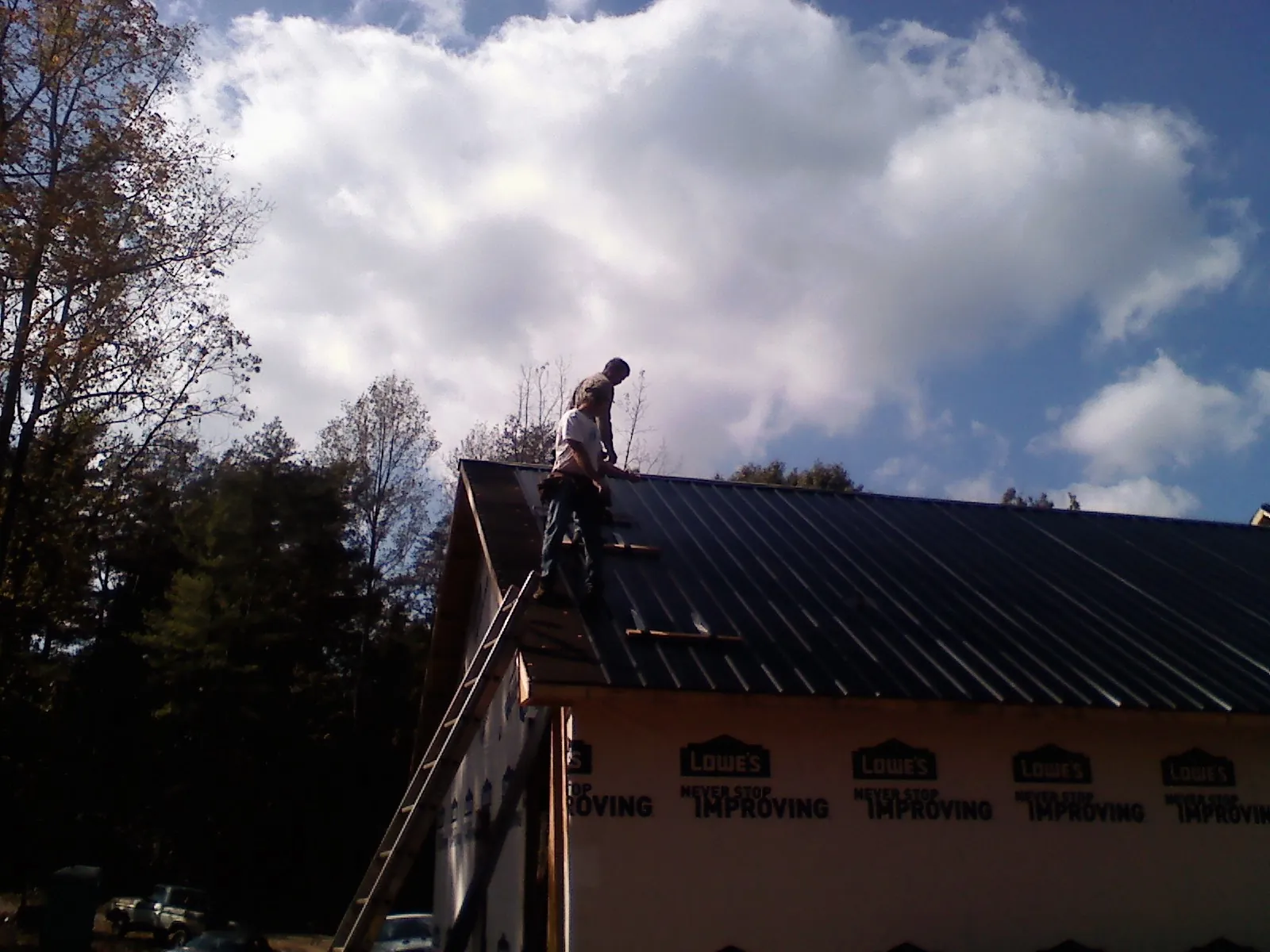 Roofer fastening dark metal panels high against a cloudy sky, from a Roof Inspection job in North Plains