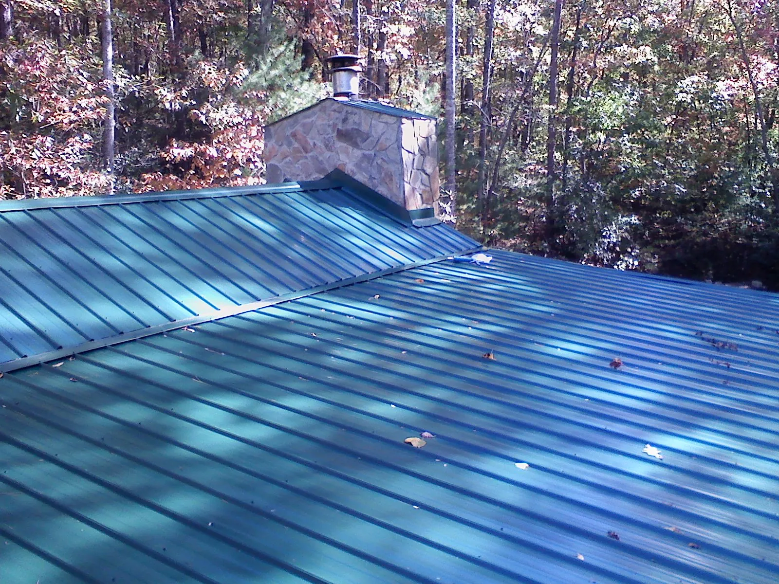 New green metal roof and stone chimney surrounded by autumn woods in North Plains