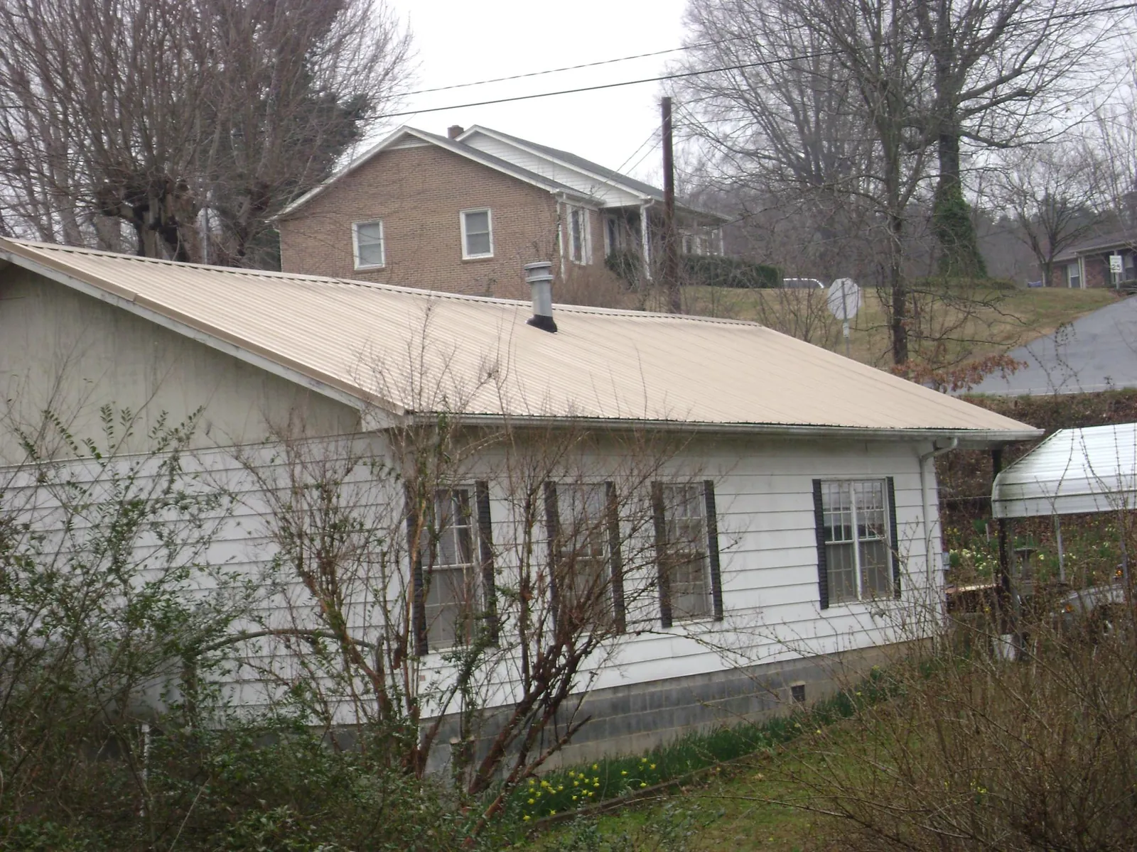 Tan metal roof on a white sided house set into a hillside — Commercial Roofing by Roofing Brothers in North Plains